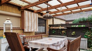 An outdoor patio with a wooden table and chairs, a hanging light fixture, and a brick wall with a window. - Apartment 'Hecke' with Shared Garden and Wi-Fi (Weddingstedt)