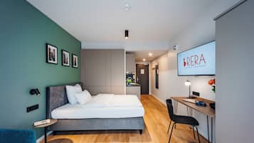 A modern bedroom with a bed, a desk, and a chair. There is a TV mounted on the wall and a framed picture on the wall.