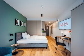 A modern bedroom with a bed, a desk, and a chair. There is a TV mounted on the wall and a framed picture on the wall. - Brera Serviced Apartments Böblingen (Boeblingen)