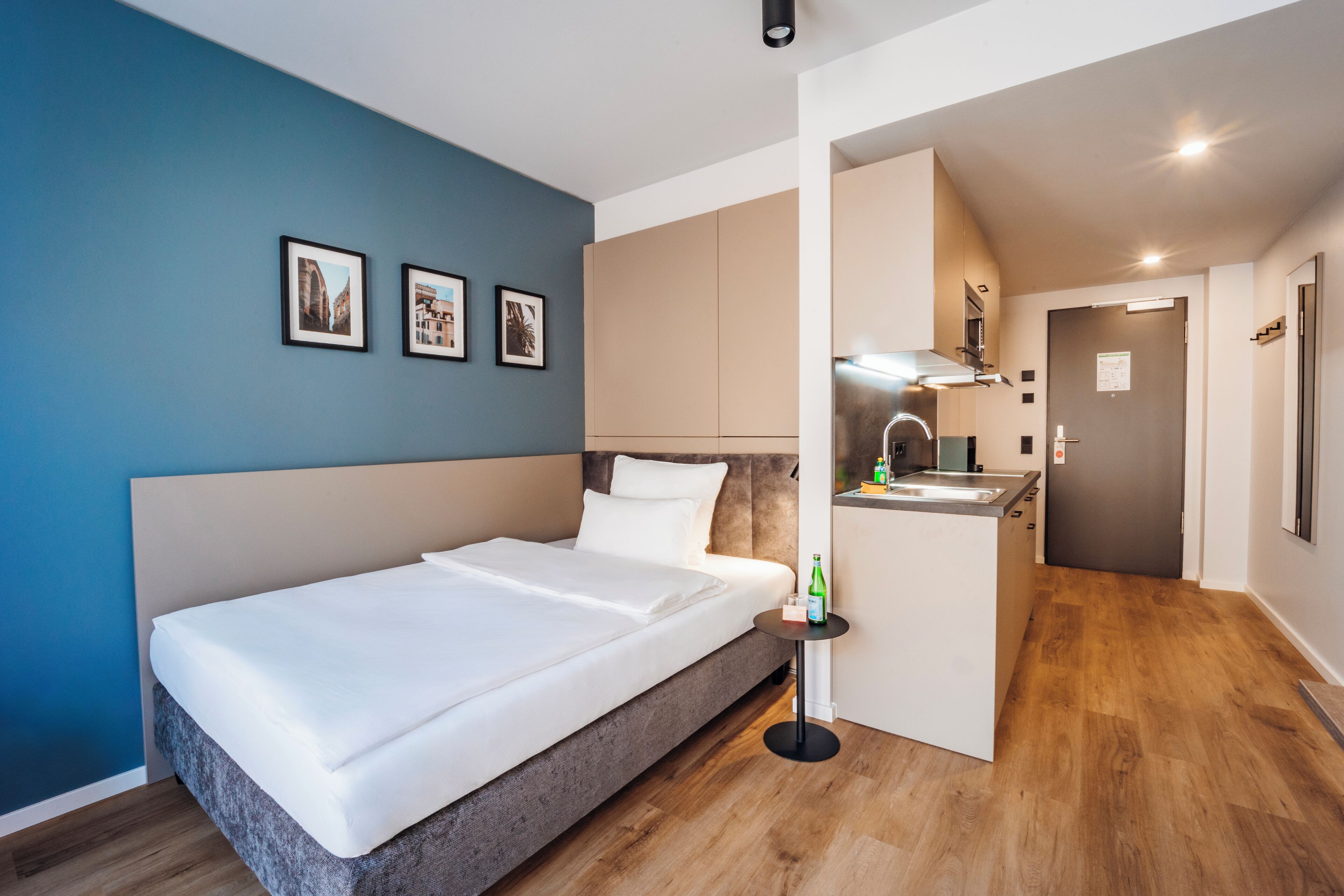 Una habitación de hotel moderna con una cama grande, una kitchenette pequeña y una pared azul de acento.