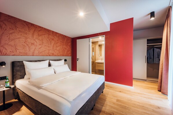 A modern hotel room with a large bed, a nightstand, a bottle of water, and a mirror. - Brera Serviced Apartments Böblingen (Boeblingen)