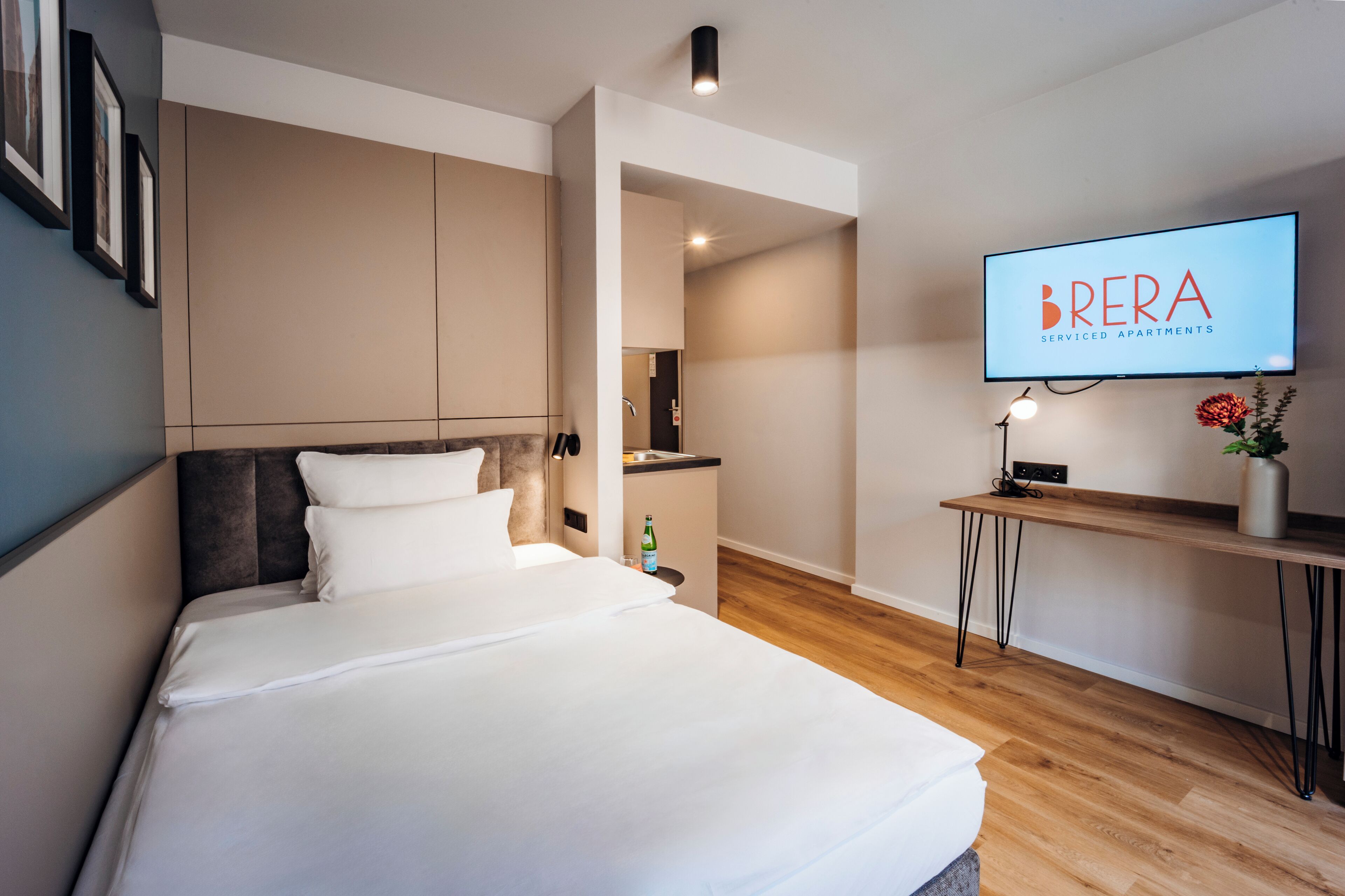 A hotel room with a bed, a desk, a television, and a wall-mounted picture frame.