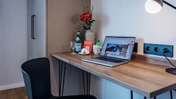 A modern workspace with a laptop, a vase with flowers, a bottle, and a mug on a wooden desk.