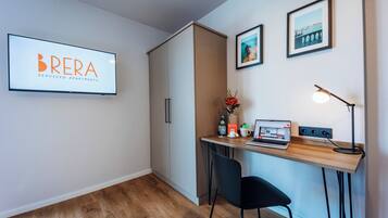 Un espacio de oficina moderno con un escritorio, una silla y una computadora. Hay un cartel enmarcado en la pared, una lámpara y un florero con flores.