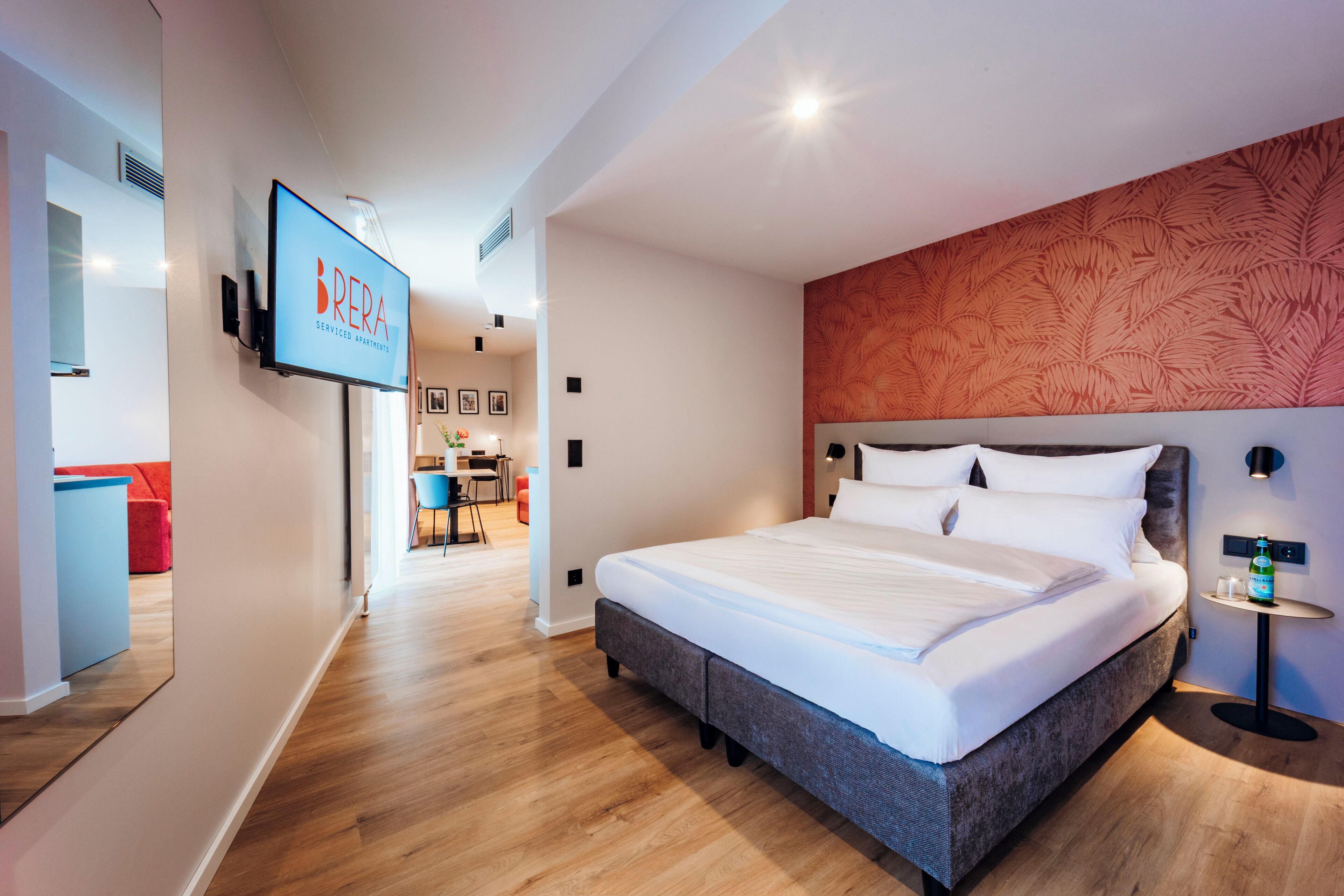 A modern hotel room with a large bed, a TV mounted on the wall, and a wooden floor.