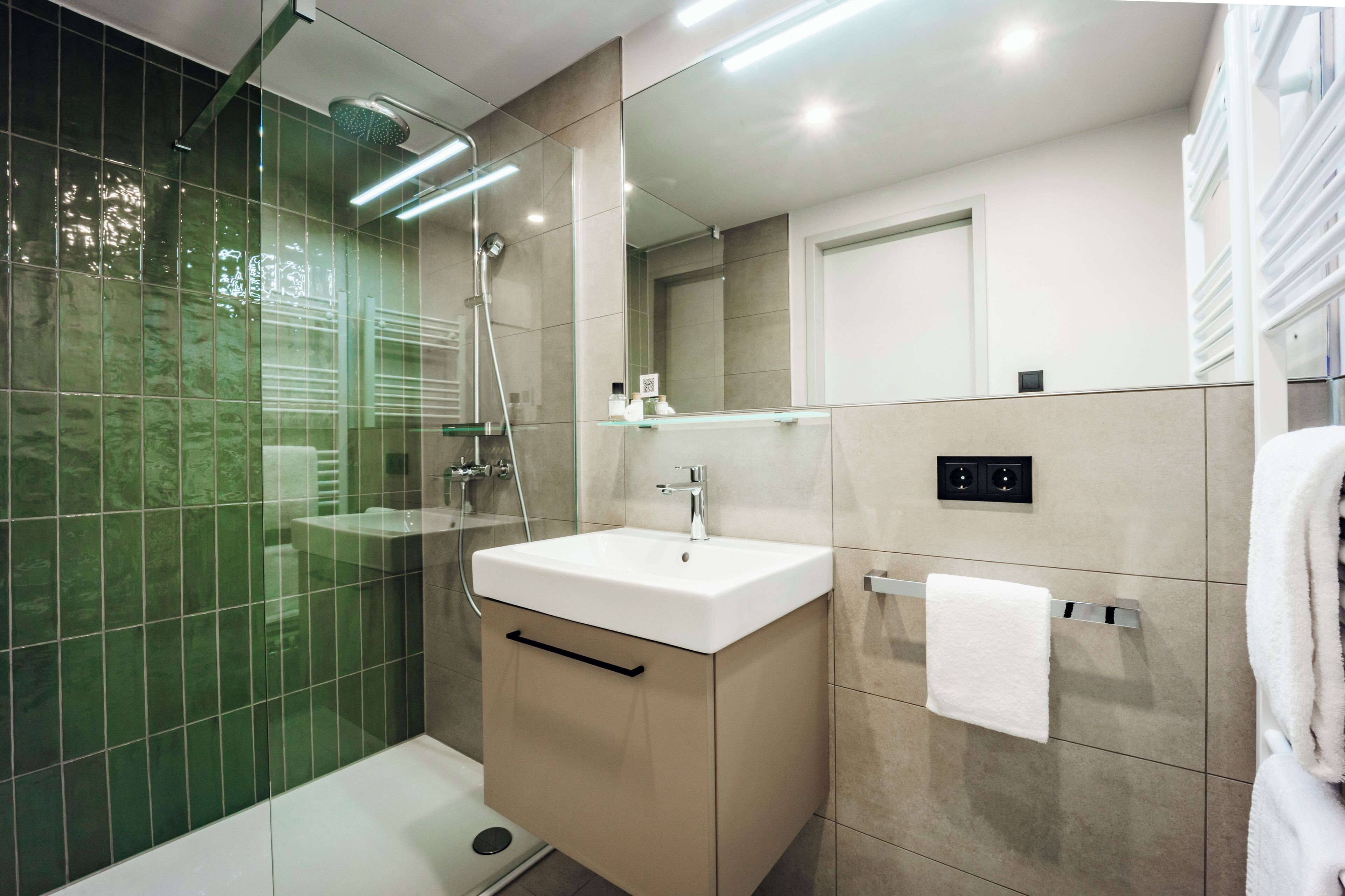 A modern bathroom with a glass shower enclosure, a white sink, and a towel rack.