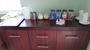 Un plan de travail de cuisine sur lequel on trouve divers objets, notamment une bouilloire blanche, une passoire en métal, des pots d’épices et des sachets de thé.