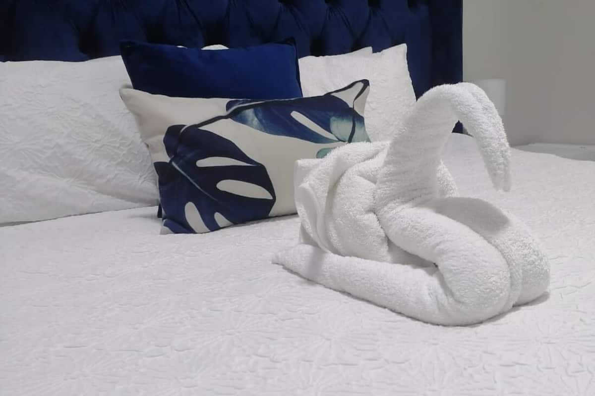 Cama bem arrumada com edredom branco e toalha decorativa em formato de cisne.