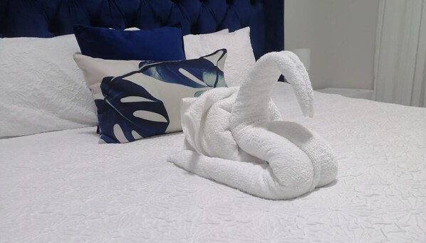A neatly made bed with a white duvet and a decorative towel shaped like a swan. - Longfellow Lodge (East London)