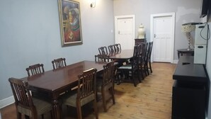 Un coin repas avec une table et des chaises en bois, un tableau accroché au mur et une lampe posée sur une petite table d’appoint.