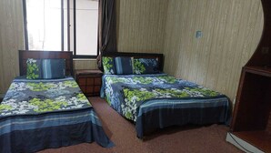 A room with two beds, each with floral bedding, a small wooden nightstand, and a window with curtains. - Sameer Guest House (Islamabad)
