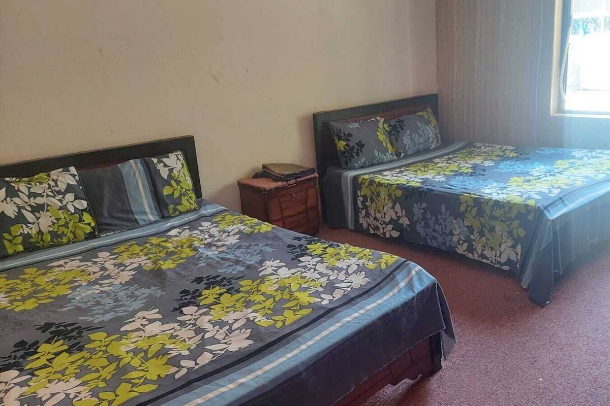 A room with two single beds, each with floral-patterned bedding, a small wooden nightstand, and a window providing natural light.
