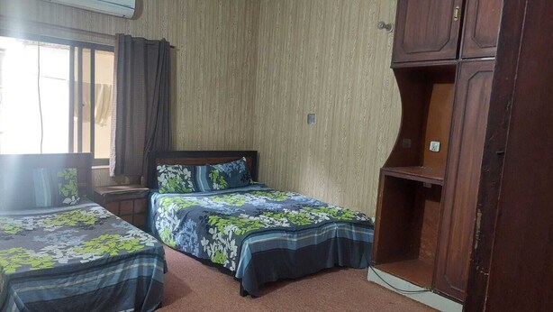 A bedroom with two beds, a wooden wardrobe, and a window with curtains. - Sameer Guest House (Islamabad)