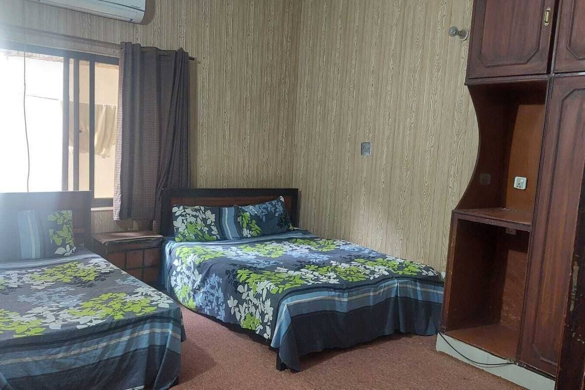 A bedroom with two beds, a wooden wardrobe, and a window with curtains.
