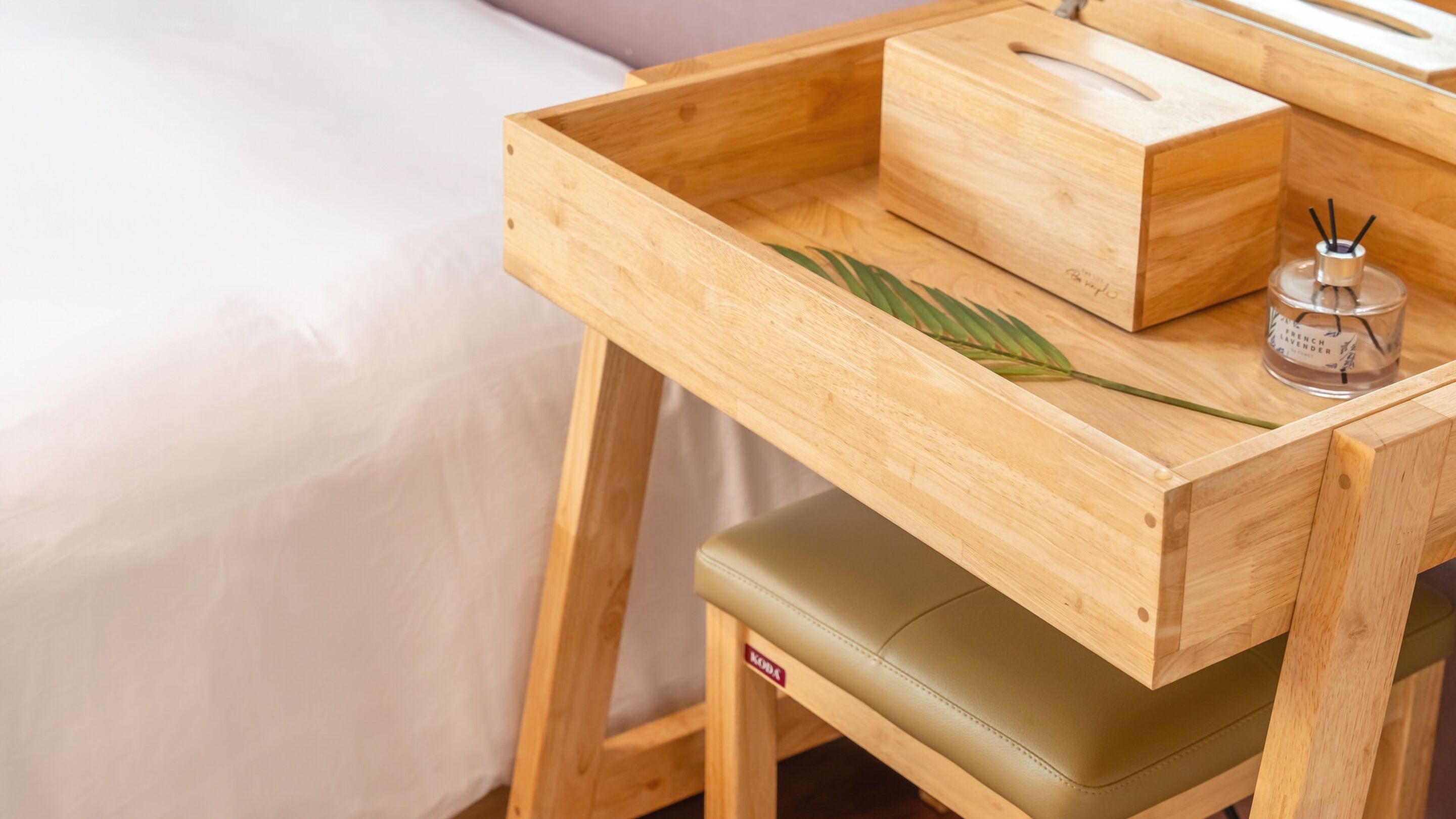 Un escritorio de madera con un cajón, un asiento acolchado verde y una botella de lavanda francesa.