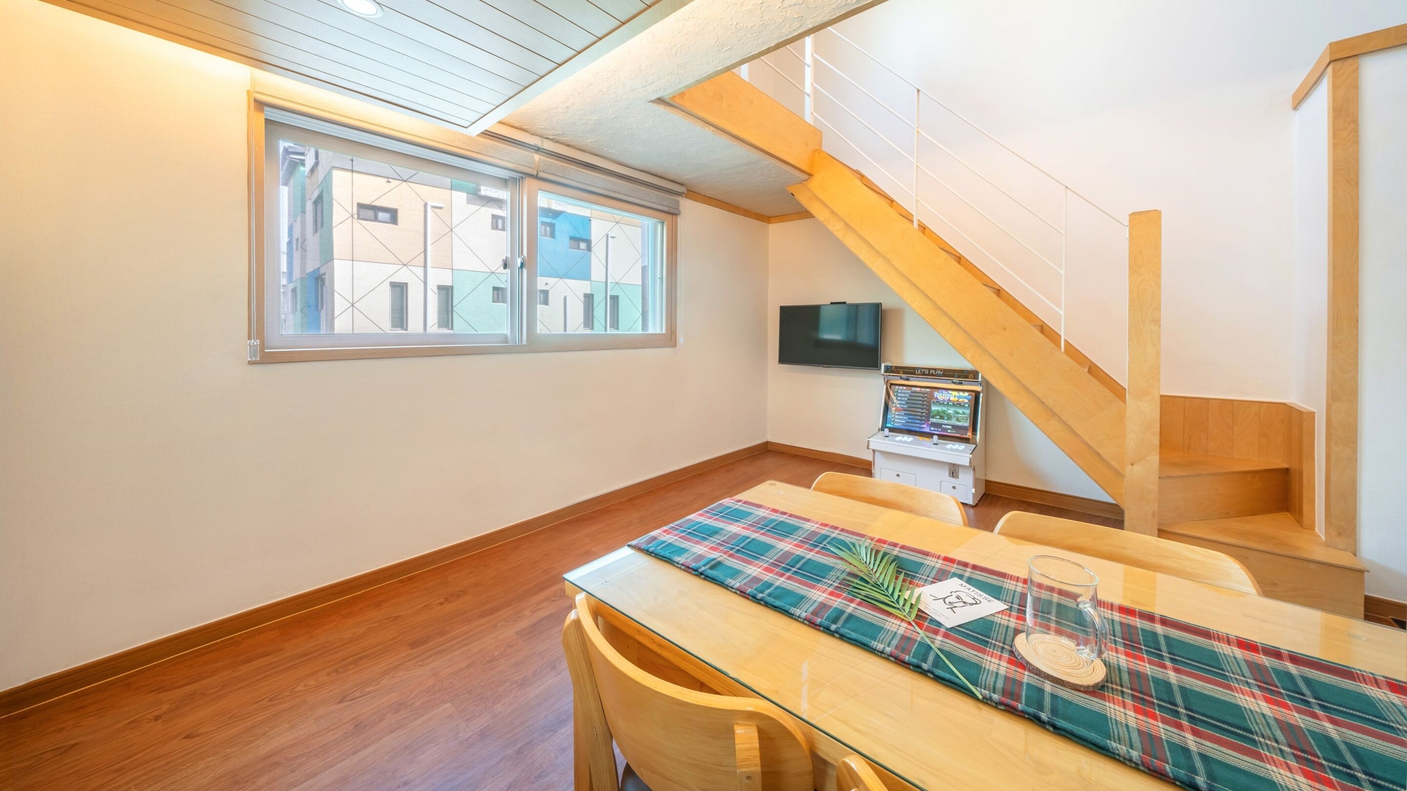 A room with a wooden table, plaid tablecloth, and a television on the wall.