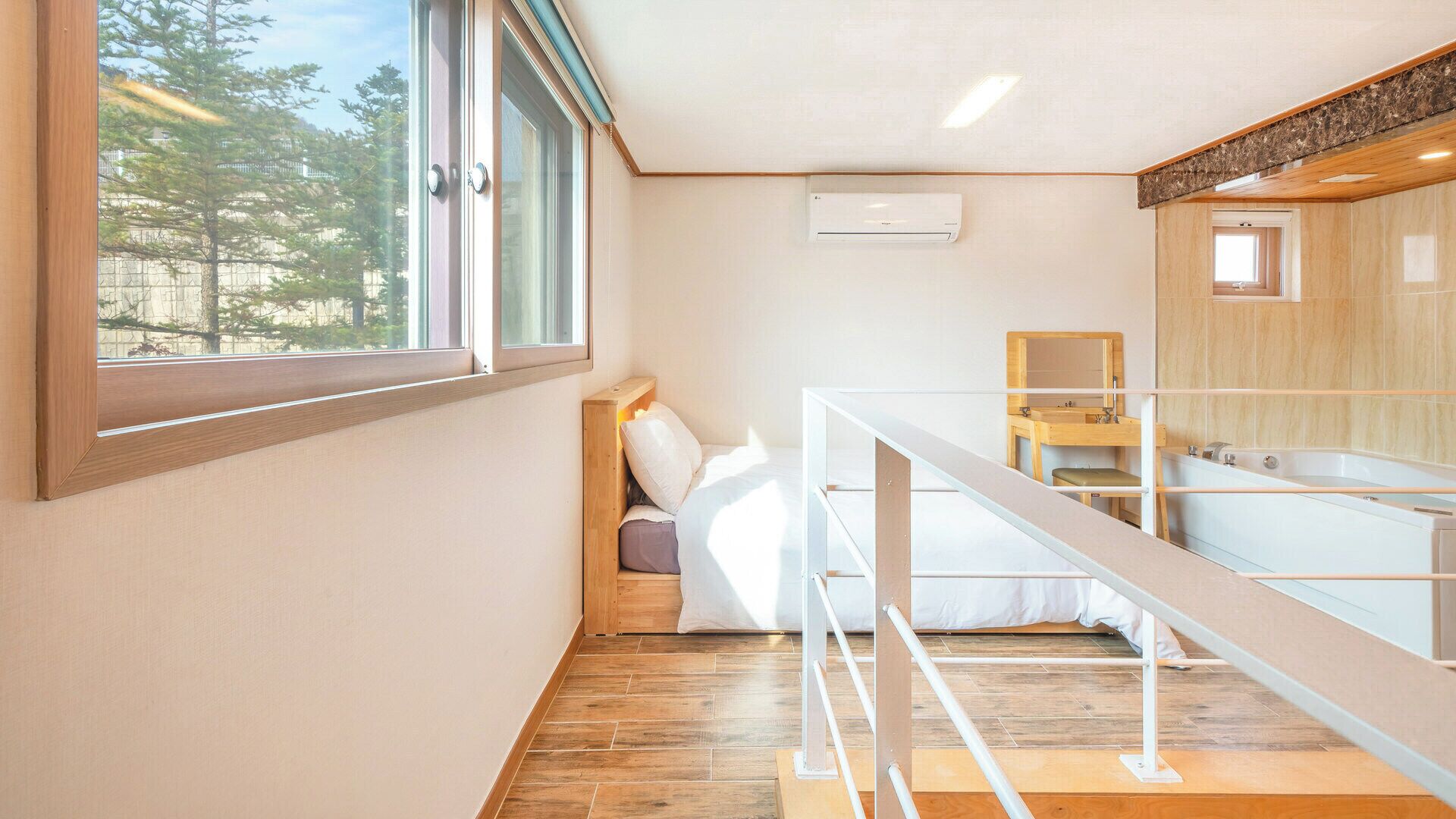 Un dormitorio con cama, ventana, aire acondicionado, piso de madera y baño con bañera.