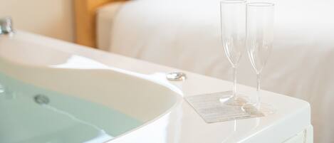 A white bathtub with two clear glasses on a white tray, a white bed, and a white wall.