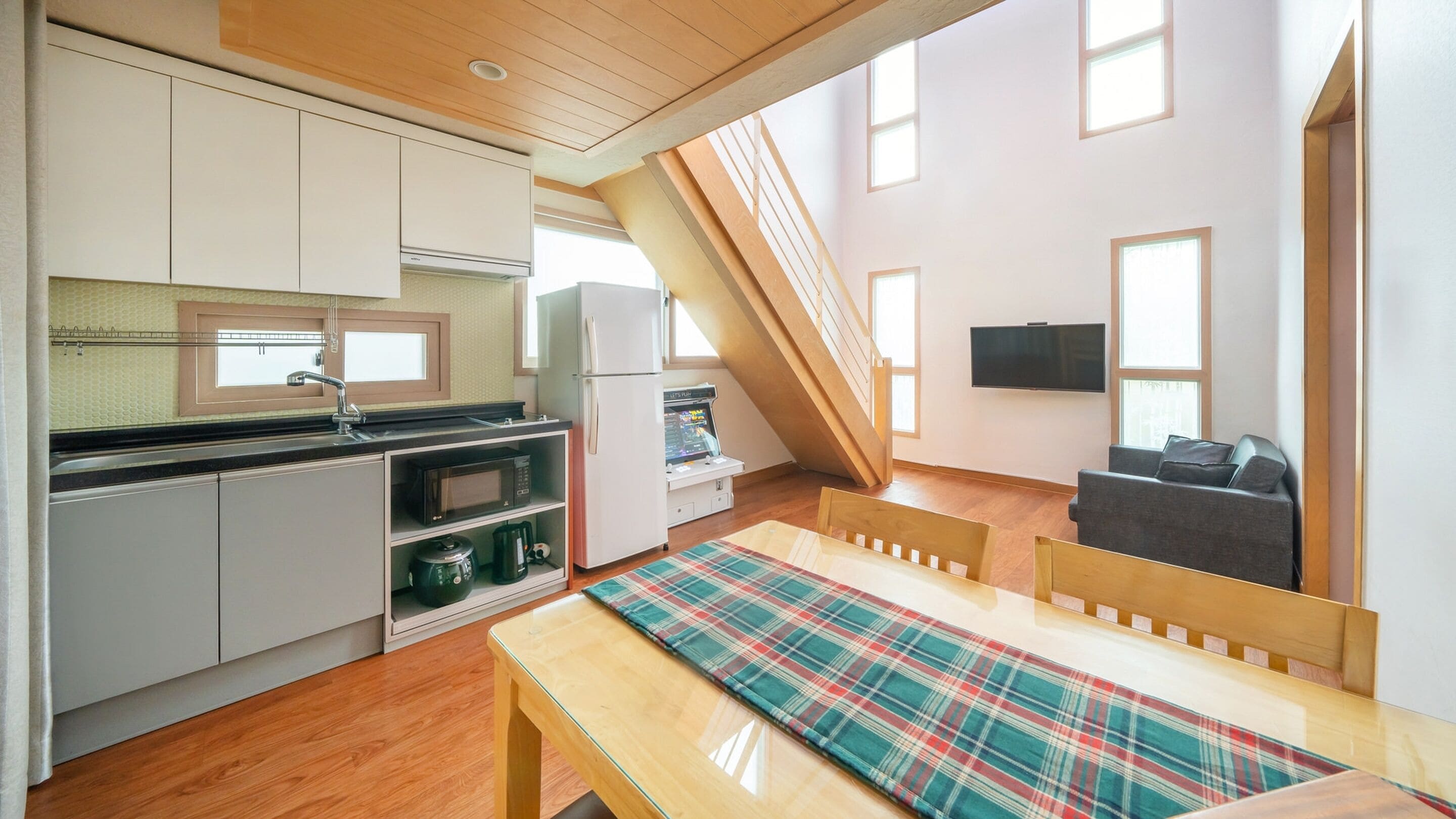 A compact kitchen with modern appliances, a dining area with a plaid tablecloth, and a TV mounted on the wall.