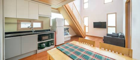 A compact kitchen with modern appliances, a dining area with a plaid tablecloth, and a TV mounted on the wall.
