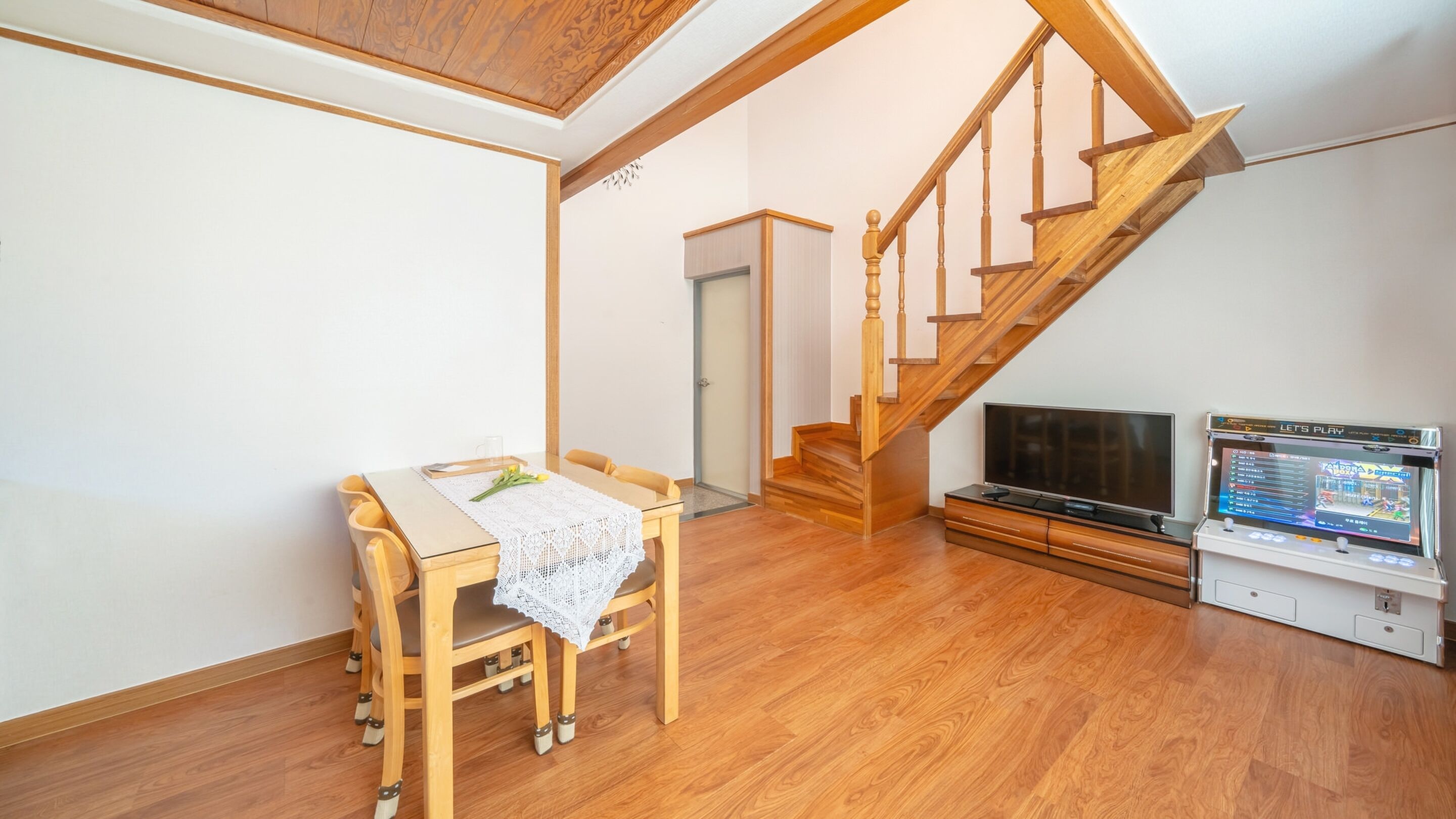 A room with a wooden dining table, chairs, a TV, and a staircase.
