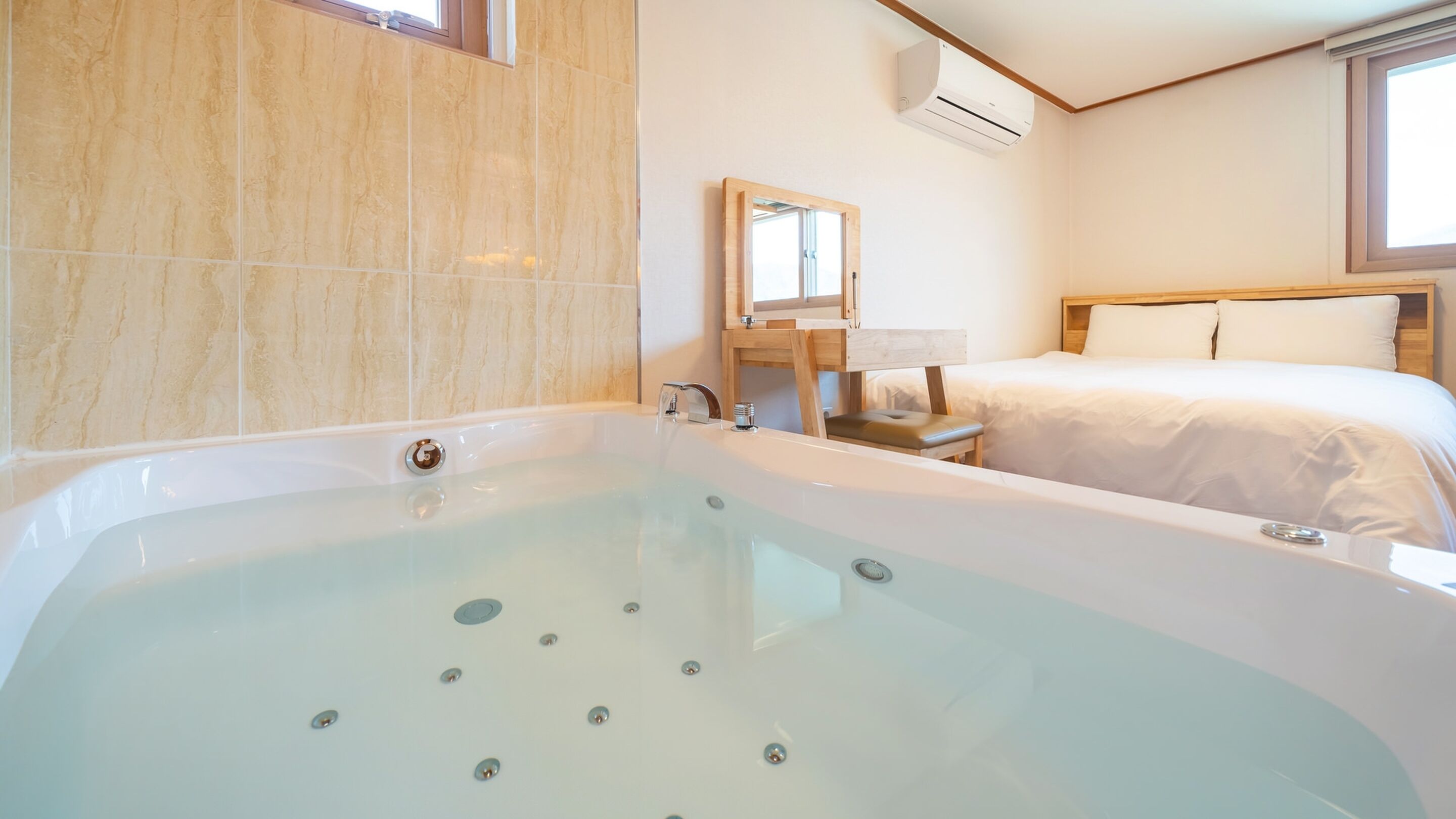 A modern bathroom with a large bathtub, a wooden-framed mirror, and a bed with white linens.