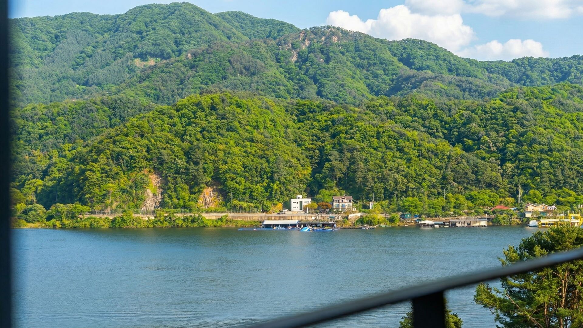 A lakeside view with a boat dock, buildings, and forested hills.
