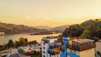Un hotel de varios pisos, un estacionamiento y vistas a un río y montañas.