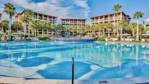 Un hotel con una piscina amplia, palmeras y un cielo azul despejado.