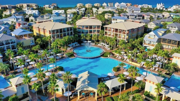 Un complejo turístico con piscina central, varias edificaciones y vista al océano.