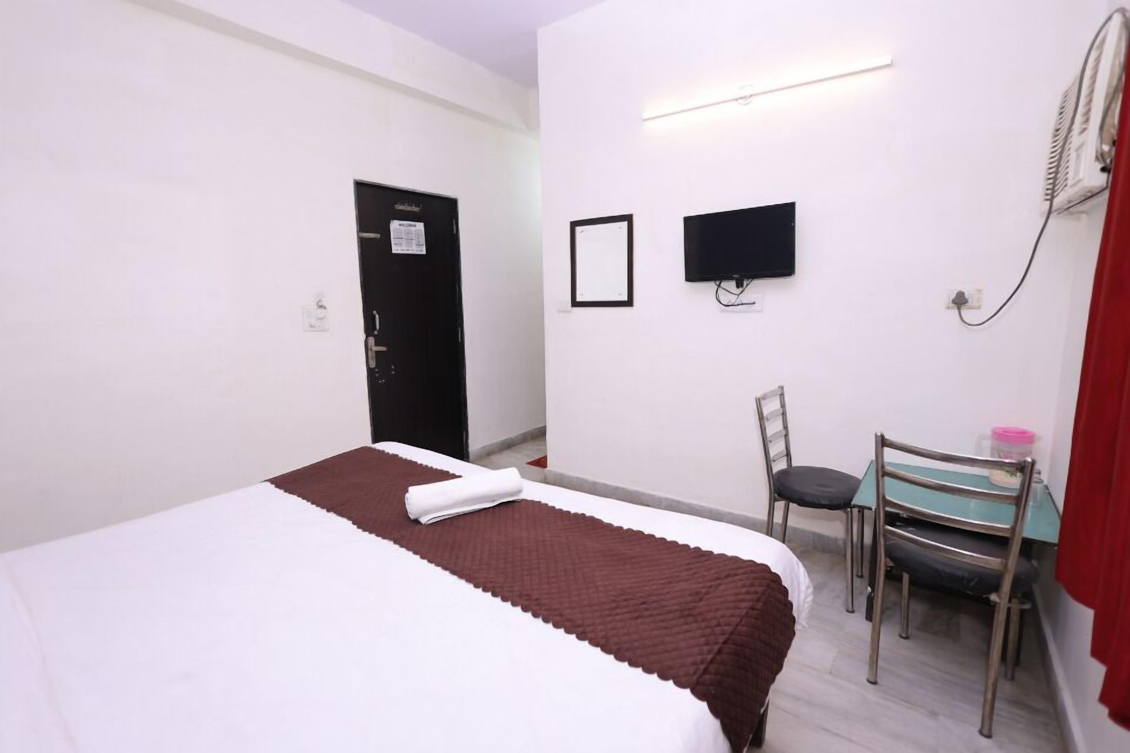A hotel room with a bed, a desk, a chair, a TV, and a door.