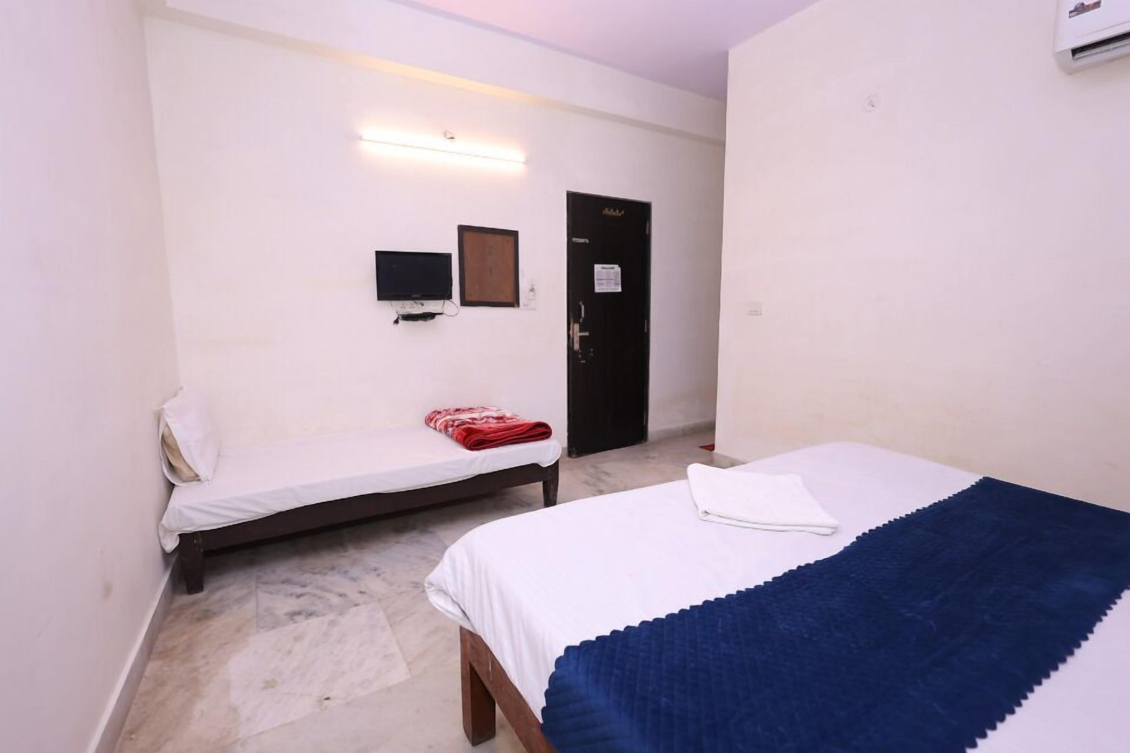 A room with a bed, a smaller bed, a flat-screen TV, a door, and a wall-mounted light fixture.