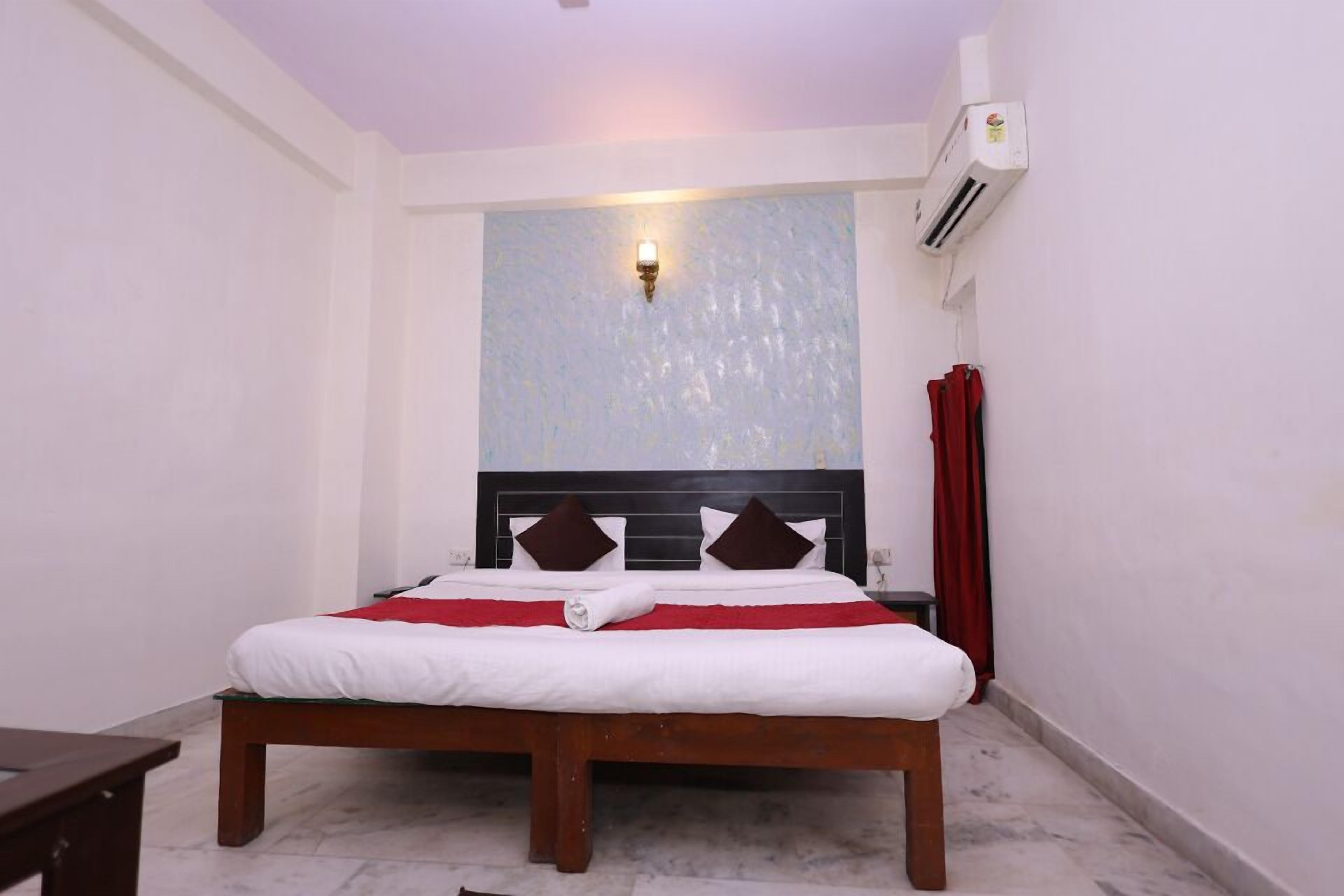 A neatly made bed with white and red bedding, a wooden headboard, and a wall-mounted light fixture.