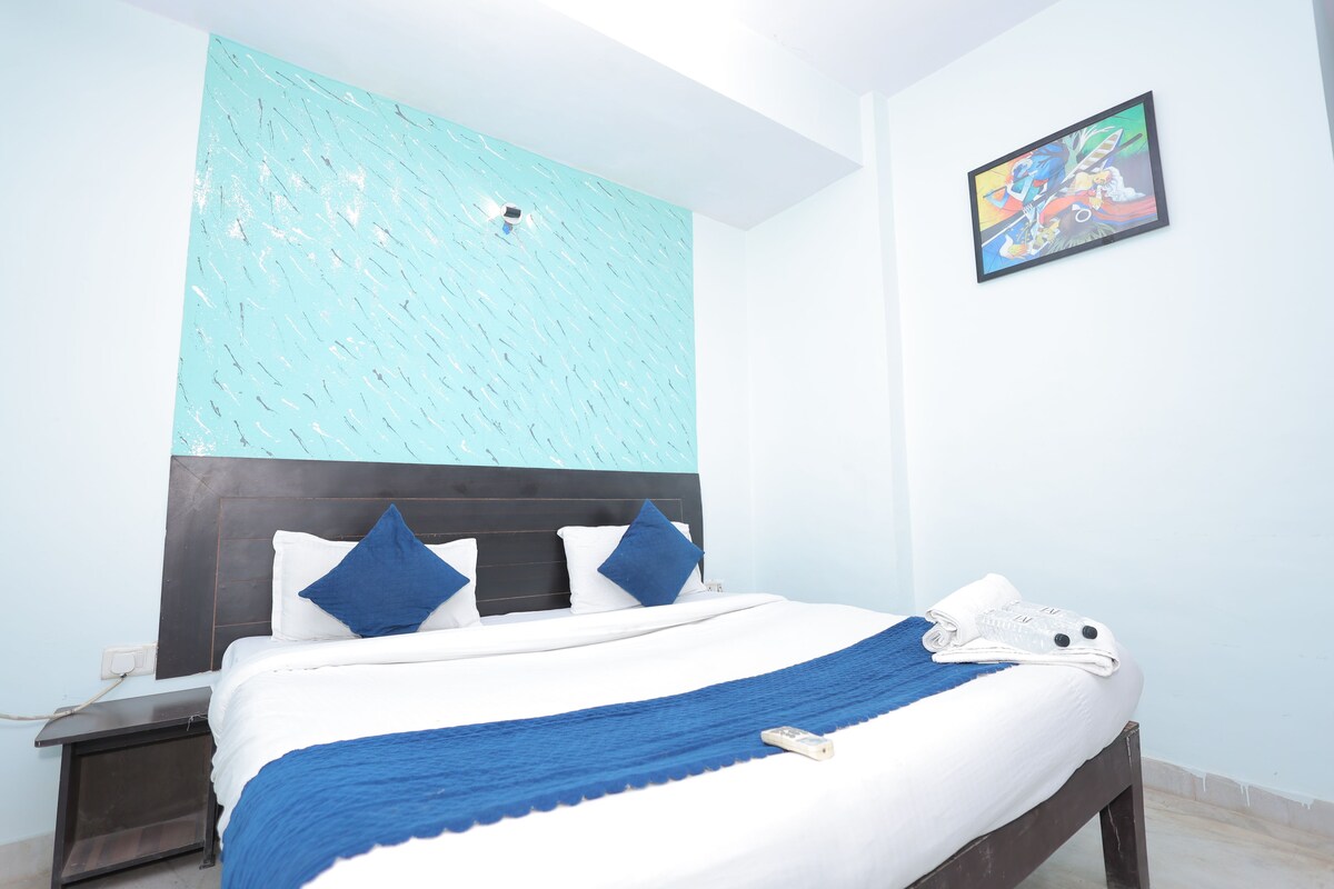 A neatly made bed with a blue throw blanket, a white pillow, and a blue pillow. There is a small white object on the bed, possibly a remote control.