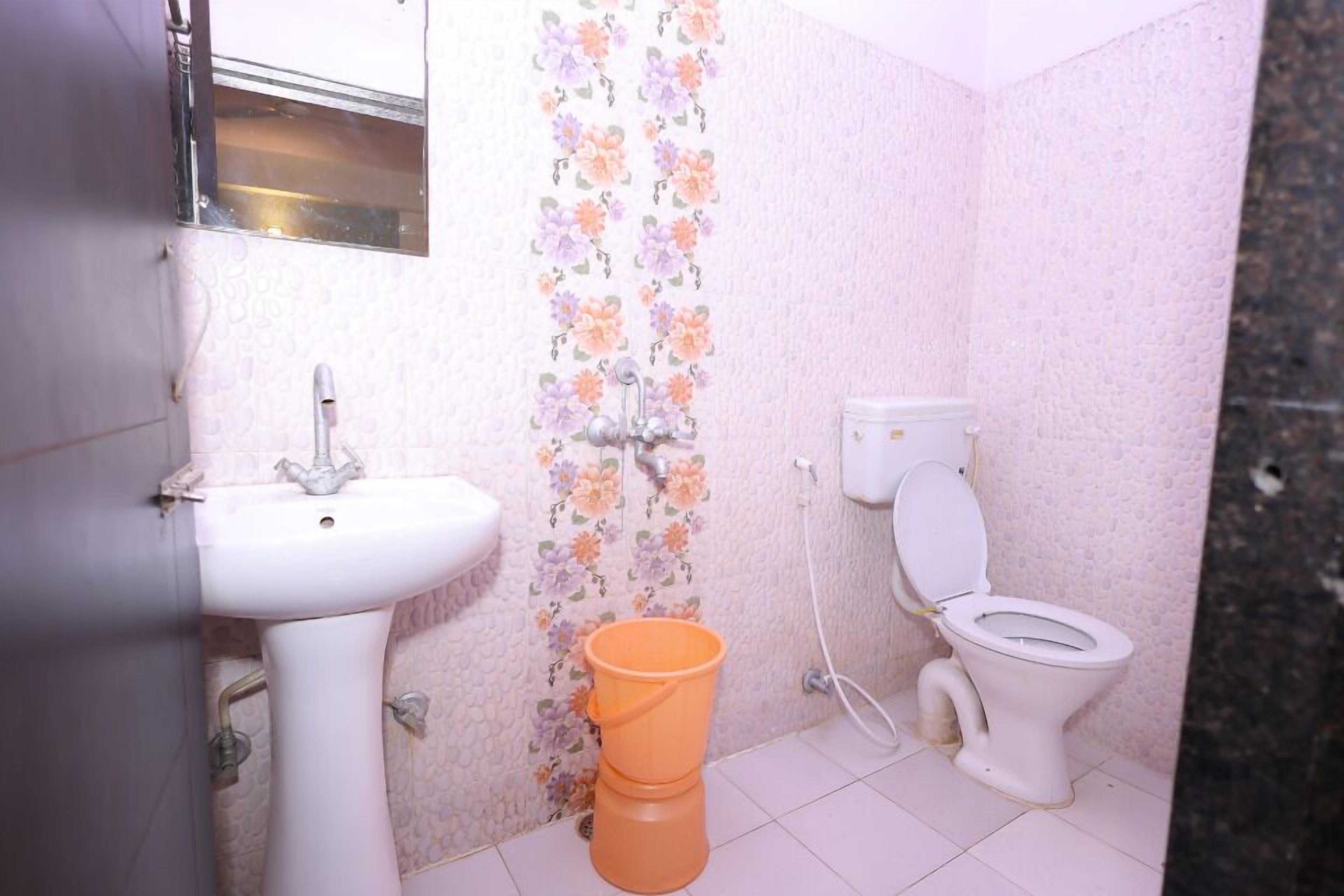 A small bathroom with a white sink, toilet, and orange bucket.