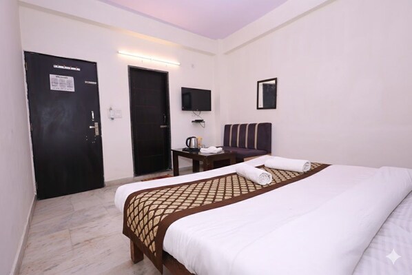 A hotel room with a bed, a television, a desk, and a door. - Hotel NoVo Agra (Agra)