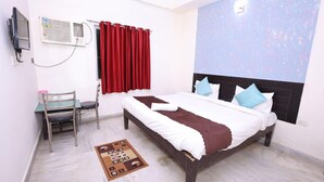 Een slaapkamer met een bed, een bureau, een stoel, een rood gordijn en een wandairconditioner.