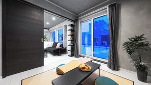 A modern living room with a large window, a sofa, a coffee table, and a potted plant. - THE SHELBOURNE FURANO (Furano)