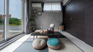 A modern room with a large window, a table with decorative items, two cushioned seating areas, and a dark wooden wall. - THE SHELBOURNE FURANO (Furano)