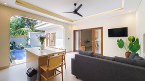 A modern living room with a sofa, dining table, and chairs, a ceiling fan, and a TV on the wall. - Gold Fish House Ubud (Ubud)