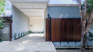 A modern entrance with a concrete pathway leading to a wooden gate, a covered area, and a wall with a door. - Gold Fish House Ubud (Ubud)