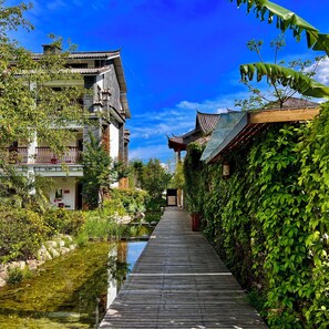 A traditional building with a wooden walkway leading to a gate, surrounded by lush greenery and a small water body. - Potala Hot Spring Resort  Dali (Dali)