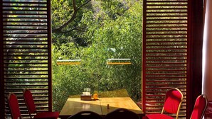 A dining area with a table and chairs, a clock, and a view of greenery through wooden slats. - Potala Hot Spring Resort  Dali (Dali)