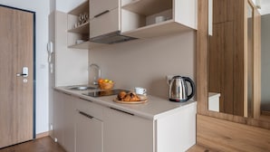 Una cucina compatta con lavandino, bollitore e angolo colazione con croissant e frutta.