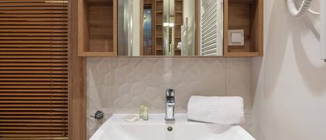 Un baño con lavamanos blanco, un espejo, un secador de pelo y persianas de madera.