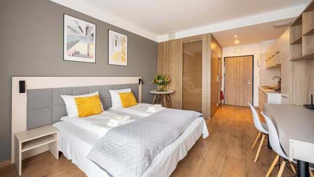 Una camera d'albergo moderna con un letto grande, comodini, un piccolo tavolino con fiori, una scrivania e un angolo cottura.