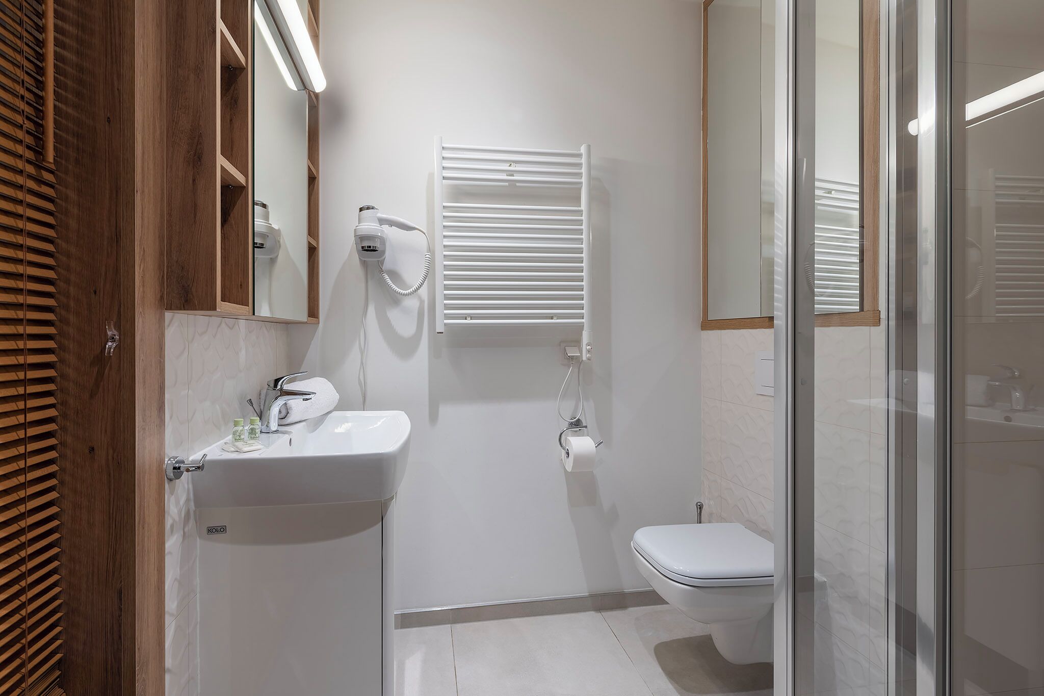 A modern bathroom with a white sink, toilet, and a glass shower enclosure.