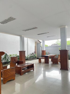 A spacious indoor area with a tiled floor, wooden furniture, and columns.
