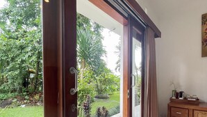Ein Zimmer mit einer Schiebetür zum Garten. Ein Holzschrank und ein kleiner Tisch mit Gegenständen darauf sind ebenfalls zu sehen.