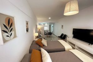 Moderni hotellihuone, jossa on vuodesohva, taulutelevisio ja taustalla ruokailutila.